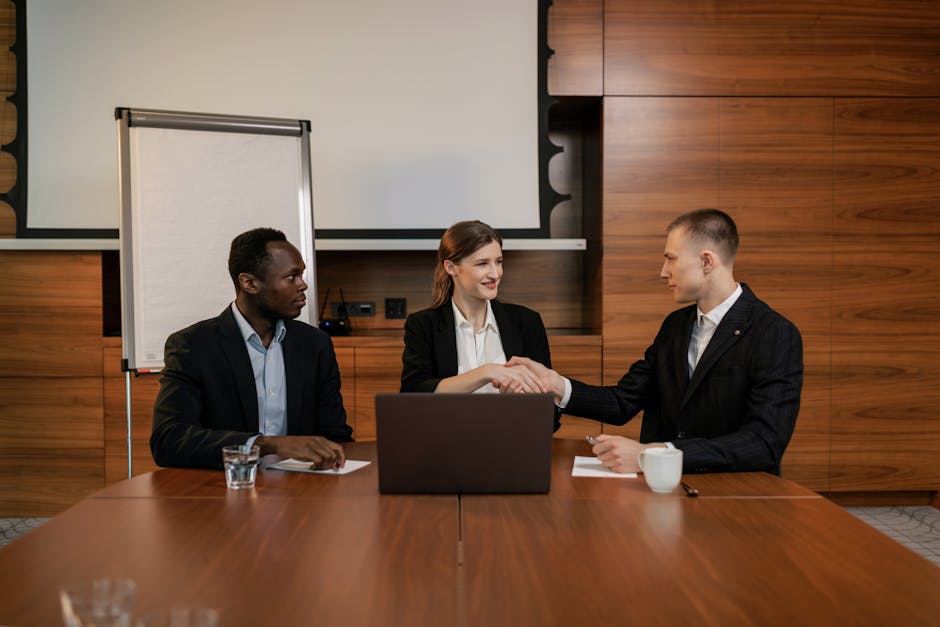 Three business professionals shaking hands during a meeting in an office.