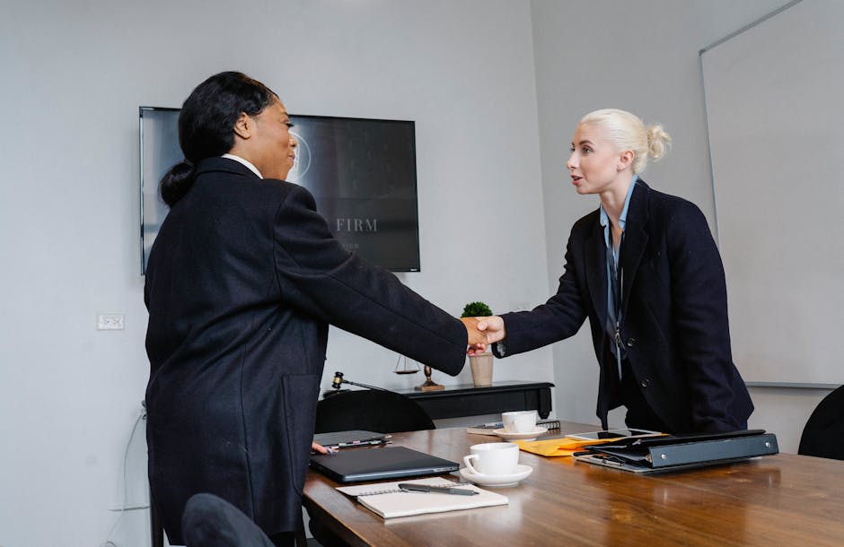 Two businesswomen shaking hands in a corporate office setting, symbolizing success and collaboration.
